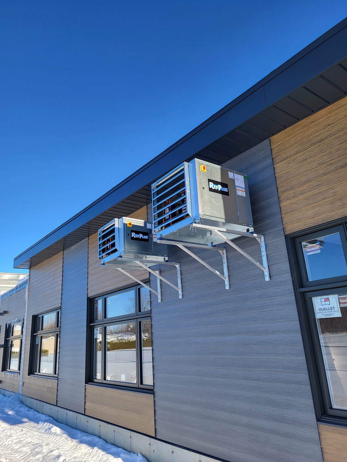 Two wall-mounted refrigeration units installed on the exterior of a commercial building in winter.