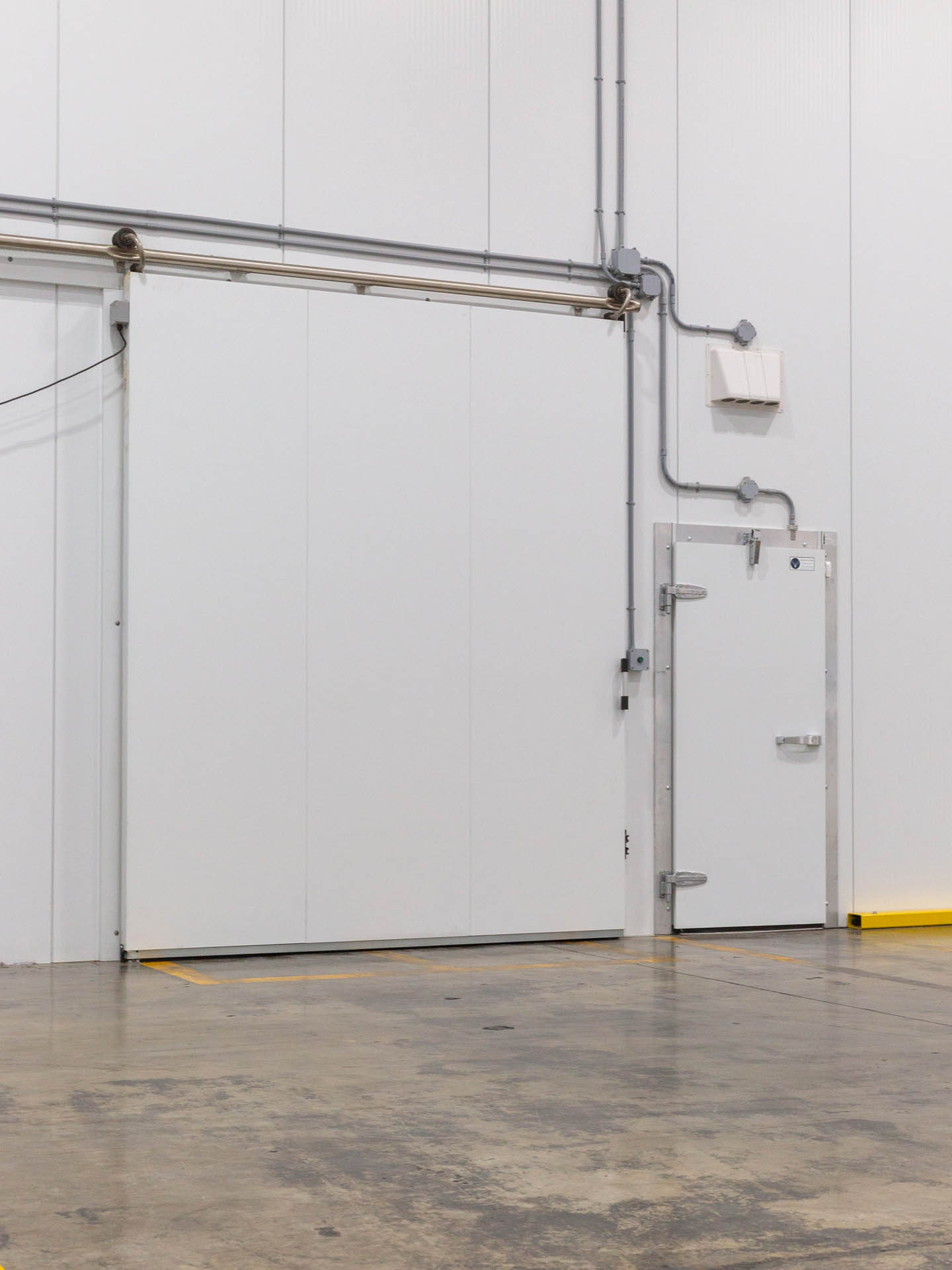 Large sliding door and standard access door for cold storage in an industrial warehouse.