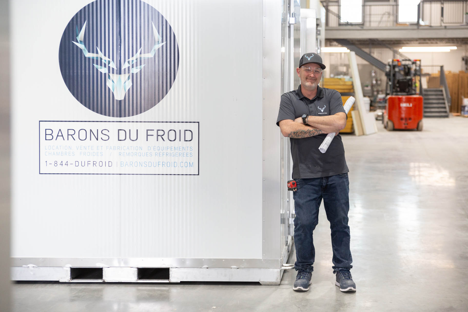 Barons du Froid employee leaning on a refrigeration unit in an industrial warehouse.